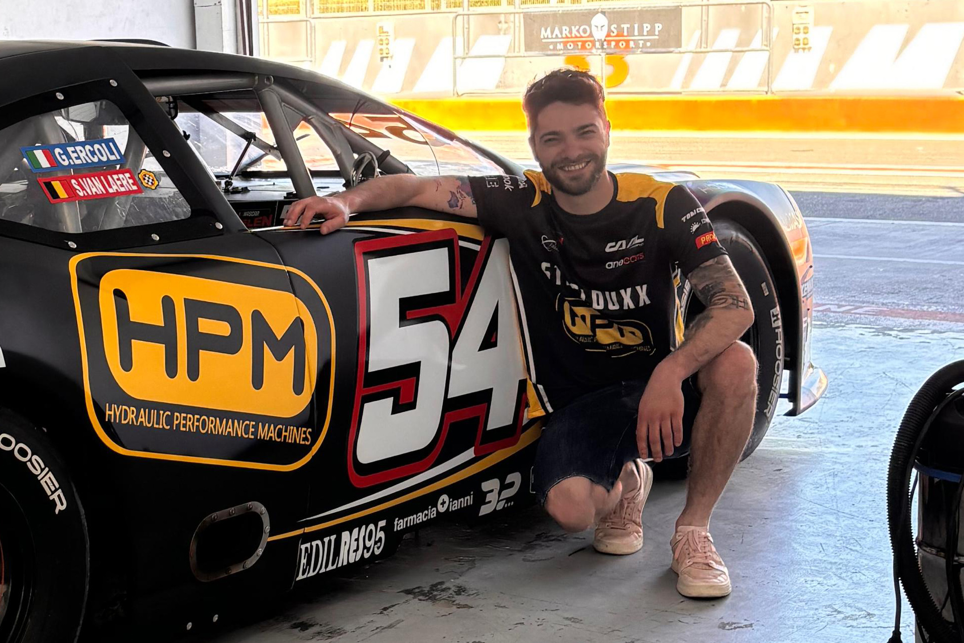 Giovanni Cartechini squats alongside the #54 CAAL Racing Chevrolet Camaro that was sponsored by HPM, his family company
